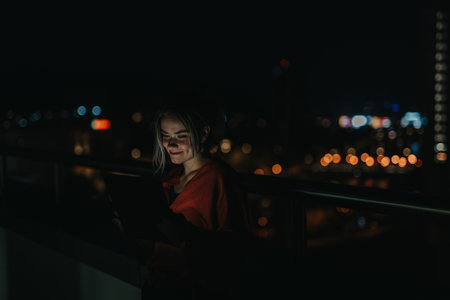 Young woman using tablet at night on a city rooftop terrace