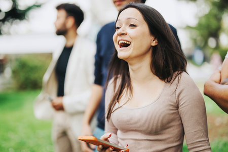 Young student laughing with friends in a park settingの写真素材