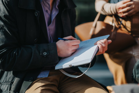Person writing notes in a notebook during a sunny day outdoor meetingの写真素材