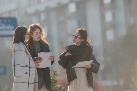 Three women discussing documents outdoors during a sunny dayの写真素材