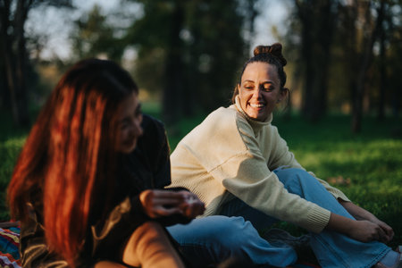Two friends laughing together in a park during a sunny afternoonの写真素材