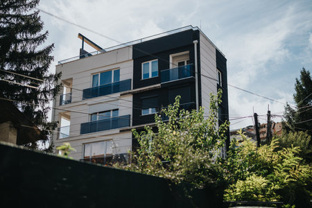Modern residential apartment building surrounded by lush greenery and a clear skyの写真素材