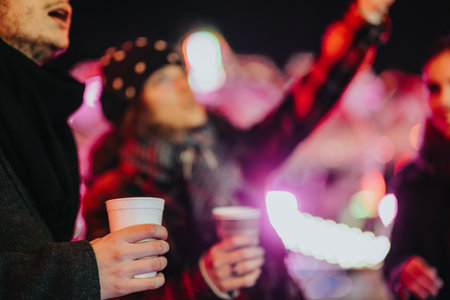 Friends enjoying warm drinks together during festive winter evening outdoorsの写真素材