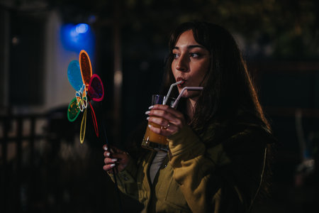 Woman at a festive celebration drinking juice holding colorful pinwheel