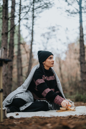 Woman sitting on a blanket during a serene winter picnic in a forested mountain areaの写真素材