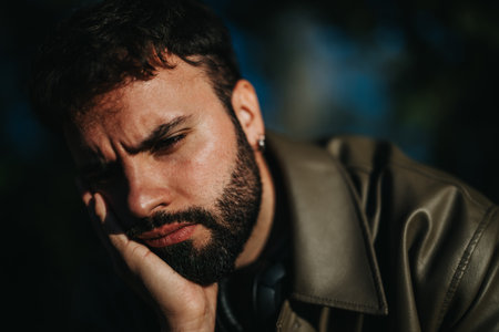 Man with thoughtful expression outdoors in natural lighting, wearing leather jacketの写真素材