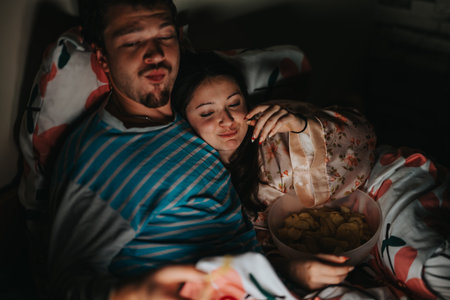 Couple enjoying cozy movie night with snacks in bedの写真素材