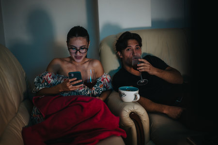Couple relaxing on sofa with drinks and smart phone in cozy settingの写真素材