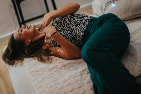 Woman joyfully lying on the couch illuminated with string lightsの写真素材