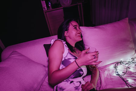 Woman laughing while relaxing at home in cozy vibrant lighting setting