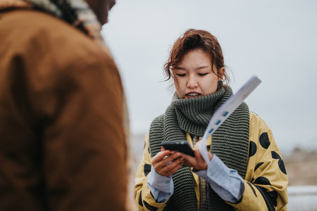 Young woman outdoors focusing on smart phone and holding a paper documentの写真素材