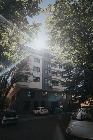 Modern apartment building with parking and sunlight filtering through trees