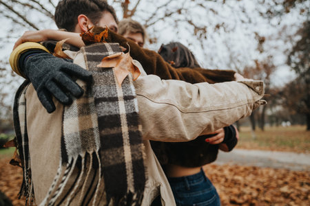 Group of friends hugging outdoors in autumn with leaves and scarvesの写真素材