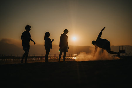 Silhouettes of friends playing on the beach during a beautiful sunsetの写真素材