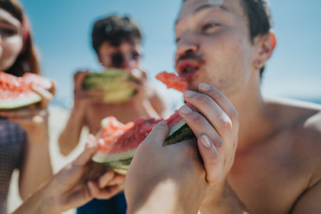 Friends enjoying watermelon slices together on a sunny summer day at the beachの写真素材