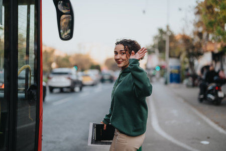 Young person smiling and waving while boarding a bus on a city streetの写真素材