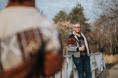 A man holding a drink while standing outdoors on a wooden bridge