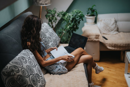 Woman relaxing on cozy sofa with laptop and notebookの写真素材