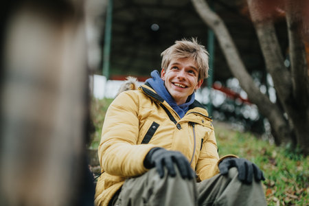 Happy young man outdoors in a yellow jacket sitting on a hillside