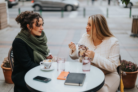 Two friends enjoying coffee and conversation at an outdoor cafe tableの写真素材