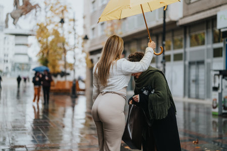 Two Women Sharing an Umbrella While Walking on a Rainy City Streetの写真素材