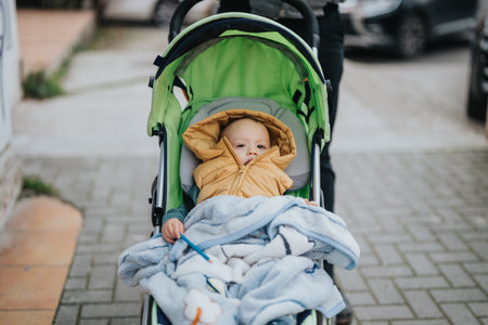 Young child in a yellow jacket sitting in a green stroller outdoorsの写真素材