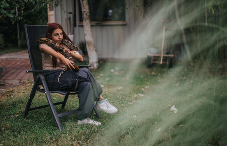 Girl calmly sitting outdoors with a large snake on her shoulders