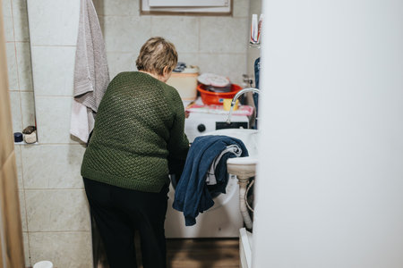 Elderly woman doing household laundry in a domestic settingの写真素材