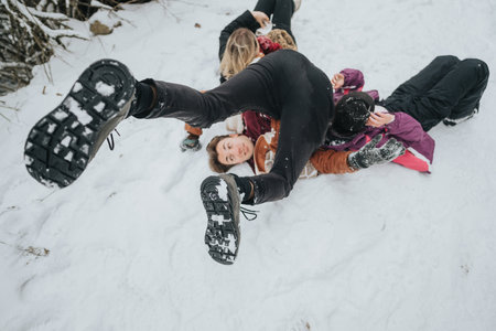 Friends playing and tumbling in the snow during a fun winter outingの写真素材