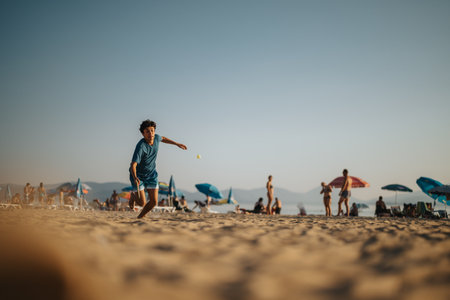 Boy playing on sandy beach with people in the backgroundの写真素材