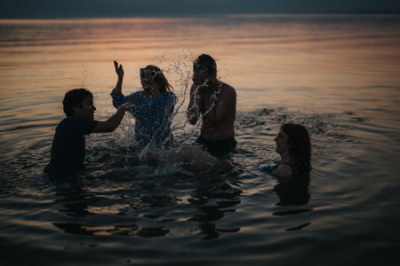 Friends having fun splashing water together in a serene sunset lake sceneの写真素材