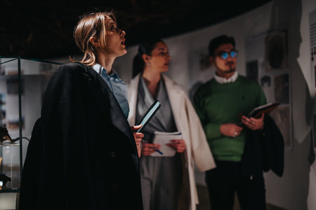 Three people attentively exploring an engaging museum exhibit with notebooks in handの写真素材