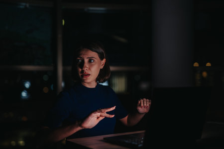 Woman working late at night looking surprised at the office computerの写真素材