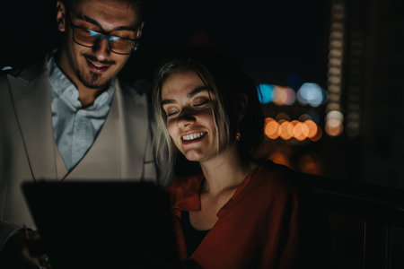 Two coworkers working together at night, using a tablet, in a casual outdoor environment.の写真素材