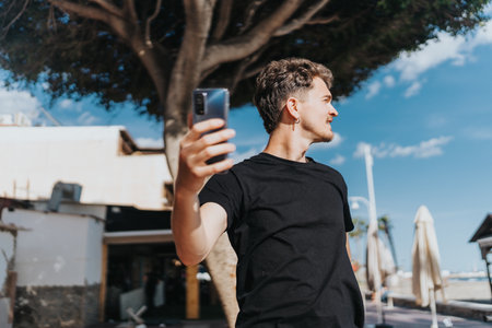 Young man outdoors in sunny Spain taking a selfie holding a smart phone.の写真素材