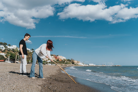 Couple cleaning up a sandy beach on a bright day with scenic viewsの写真素材