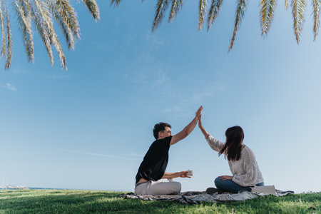 Friends high-fiving while sitting together outdoors under a clear blue sky with palm trees.の写真素材