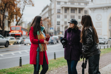 Three women dressed for autumn fashion engaged in conversation along a busy city streetの写真素材