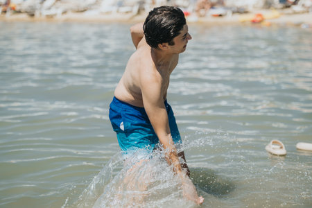 Young man splashing water while having fun at scenic lakesideの写真素材