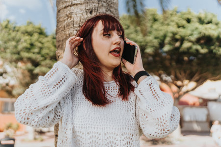 Woman in a stylish white sweater talking on a smart phone outdoors on a sunny dayの写真素材