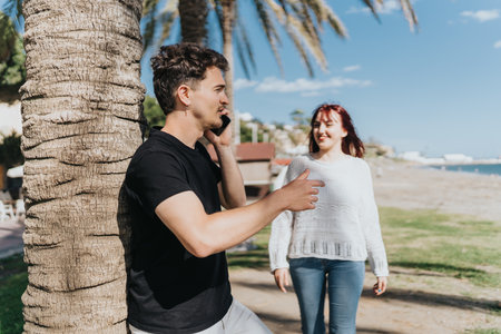 Young pair by a palm tree on a sunny day at the beach.の写真素材