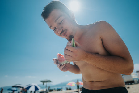 Man Eating Watermelon Under the Bright Summer Sun on a Beachの写真素材