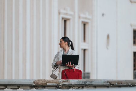 Professional businesswoman standing outdoors holding a laptop with a focused expression