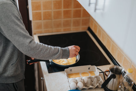 Young man cooking breakfast eggs in a modern kitchen environmentの写真素材