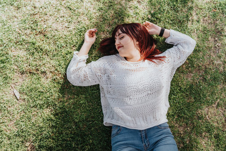 Woman enjoying relaxation outdoors on a sunny day, lying on grass