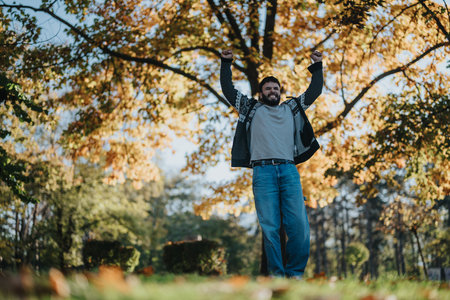 Man celebrating success in a vibrant autumn park setting with joyの写真素材