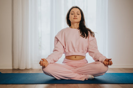 Young woman meditating in a serene indoor setting dressed in pinkの写真素材