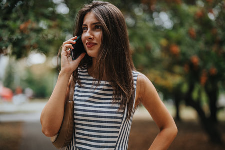 Young woman happily talking on phone in a park settingの写真素材