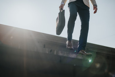 Businessperson walking down stairs holding a bag on a sunny day outdoorsの写真素材
