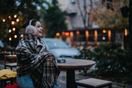 Smiling woman sitting in a cozy cafe outdoors on a chilly dayの写真素材